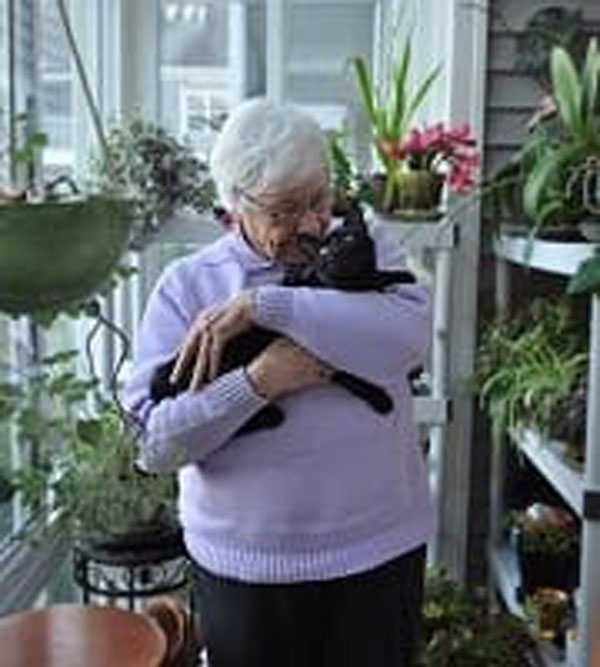 A senior woman poses with her black cat
