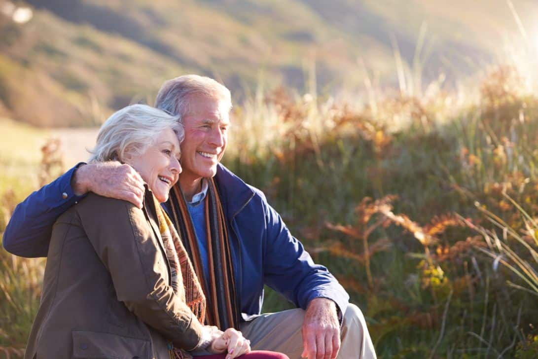 An independent senior couple sitting near a coastal path and resting during a walk.