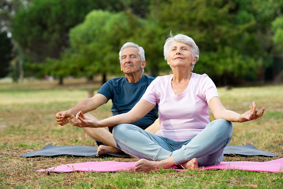 A senior couple sitting down outside on mats, practicing yoga