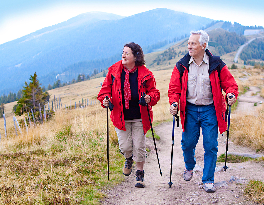 A senior couple hikes in nature using Nordic walking poles.