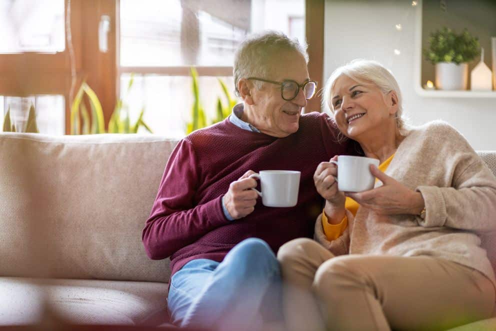 A senior couple enjoys spending time together with coffee on their couch.