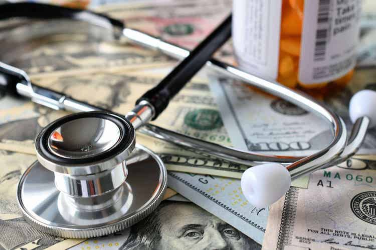 A stethoscope and medicine laying on a pile of money.