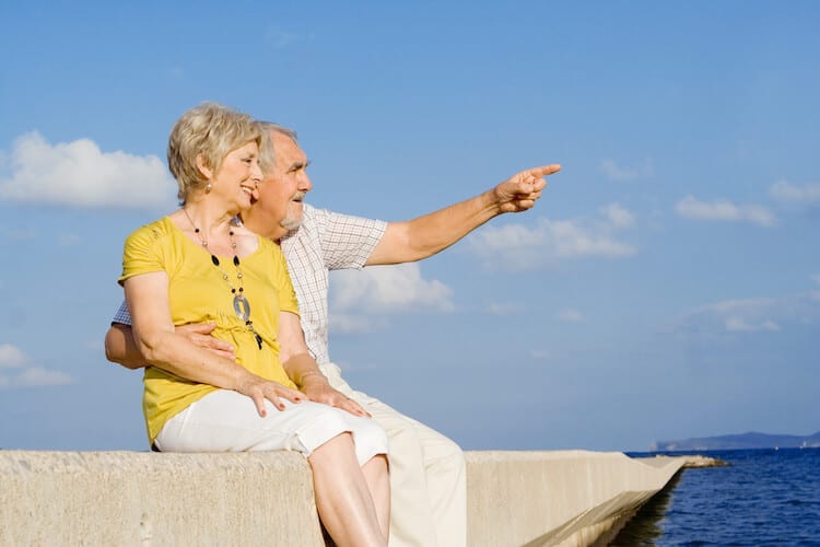 A happy senior couple sitting on a pier by the ocean.