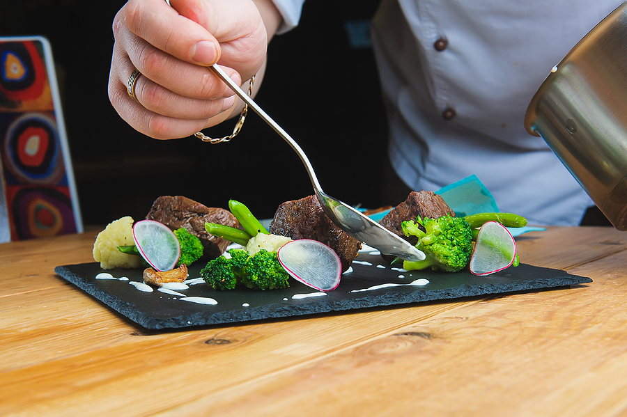 Close-up image of a chef’s hands applying the finishing touches to a dish.
