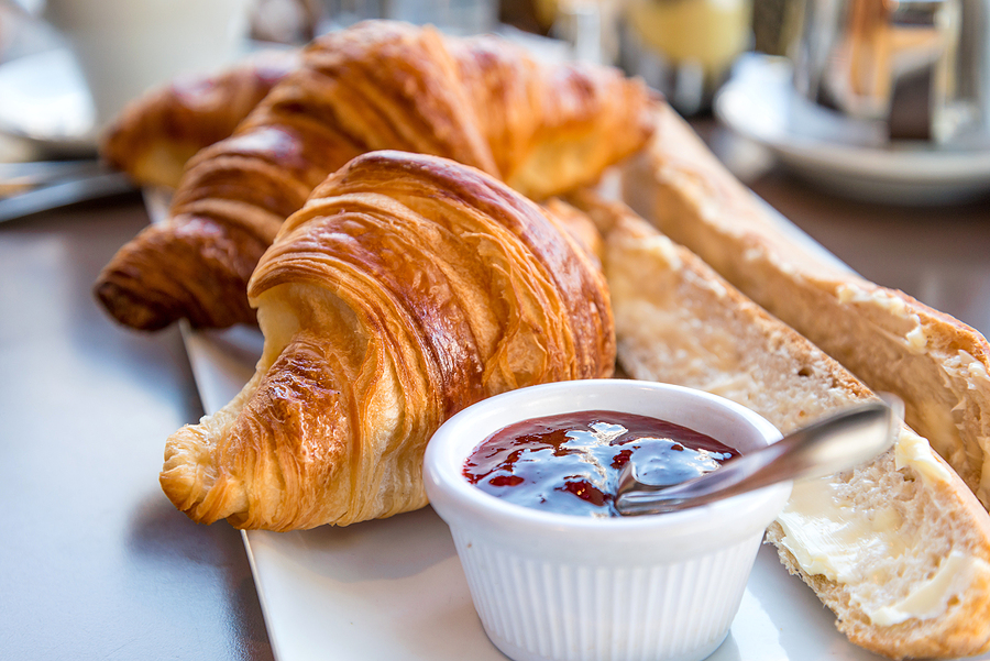 Freshly baked croissants served with a French baguette and a dish of strawberry jam on a breakfast table.
