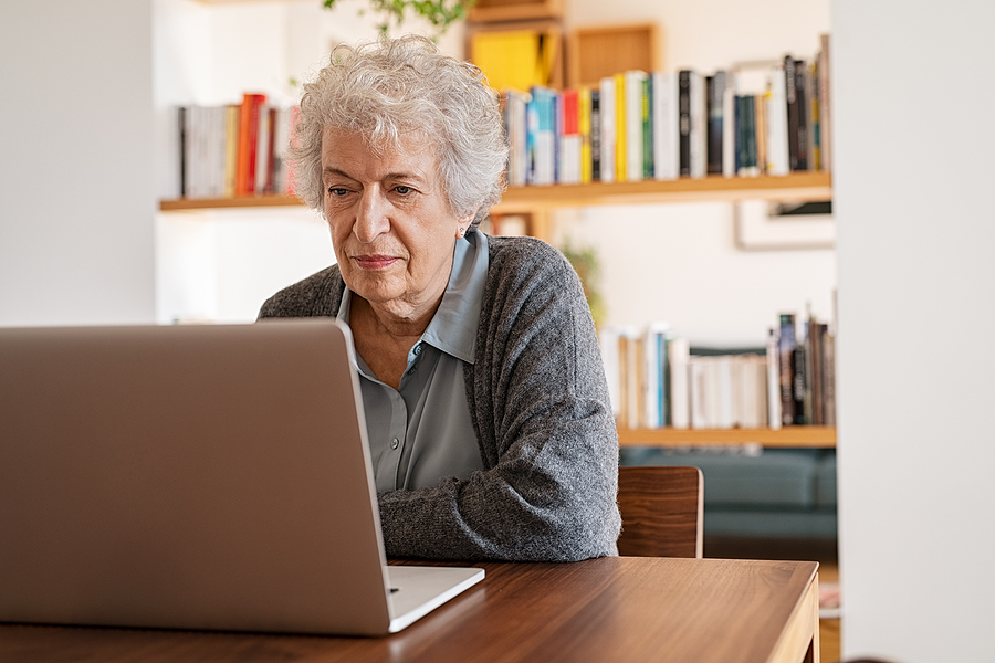 A senior woman sits at a desk on her laptop