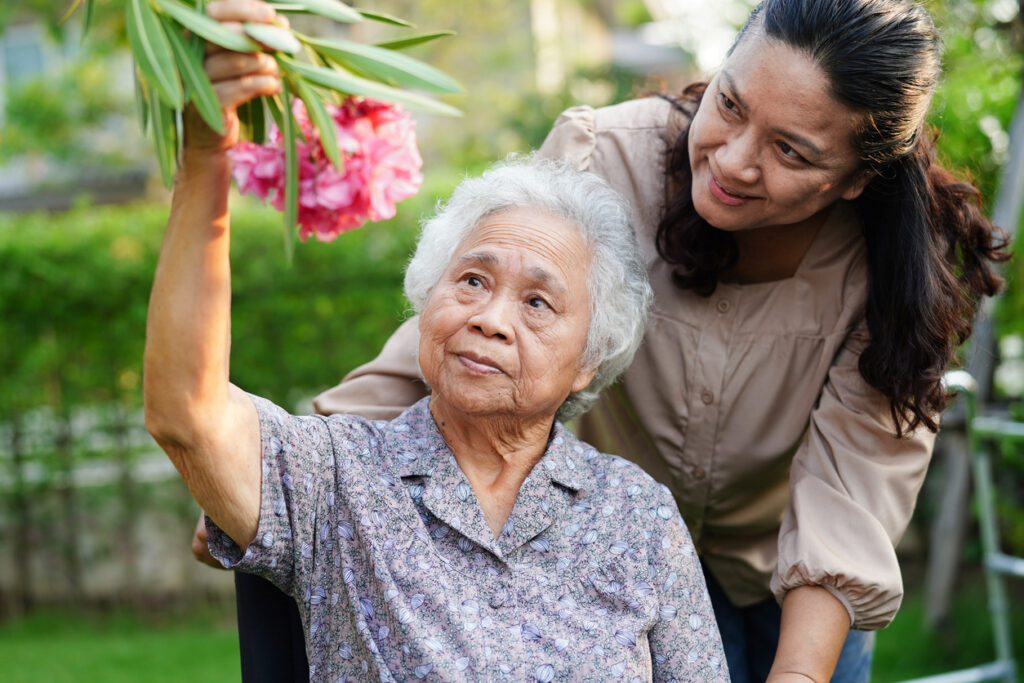 Caretaker Showing Elderly Woman Flowers Outside