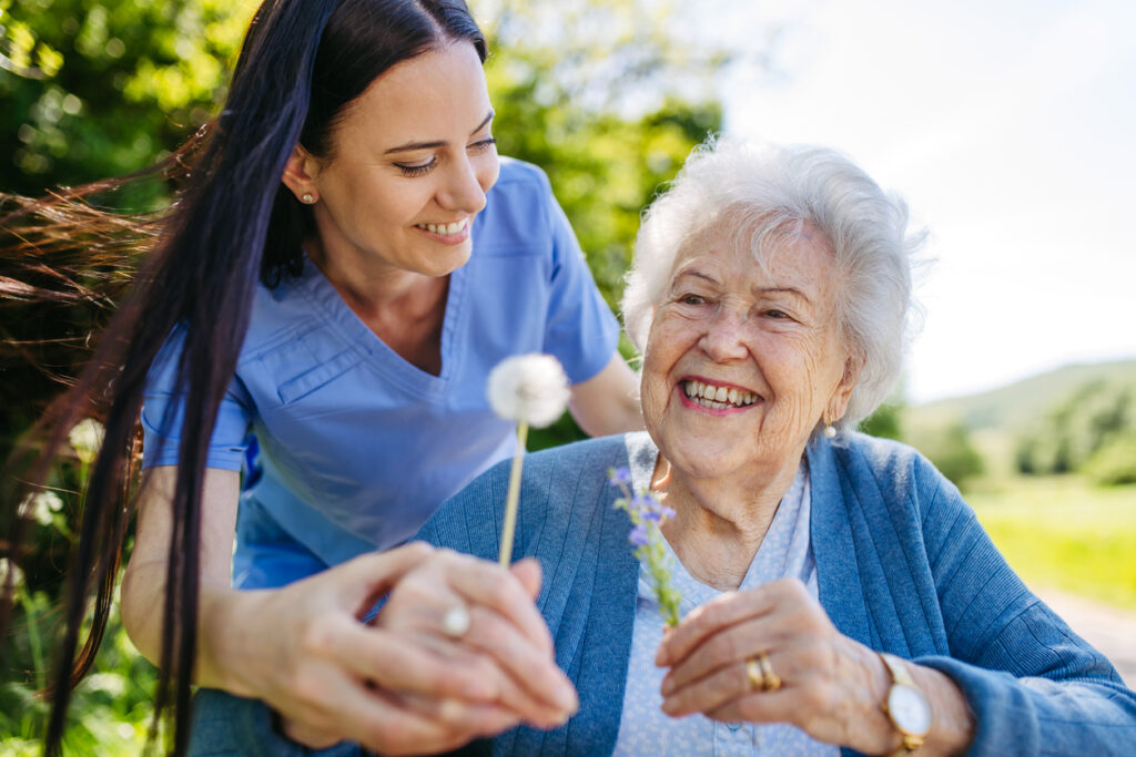 Senior Woman and Nurse Smiling Outside Looking at Flowers
